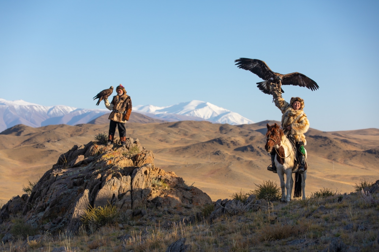 Two old traditional kazakh eagle hunters posing with their golden eagle in the mountains. Ulgii, Western Mongolia.